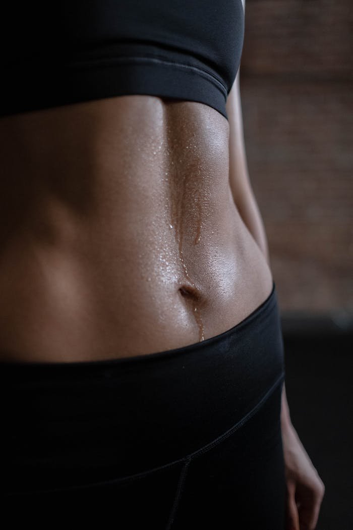 A close-up of a fit womans toned abdomen with sweat, emphasizing fitness and strength.